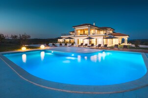 Una casa grande de dos pisos con piscina, mobiliario exterior y un patio bien iluminado.