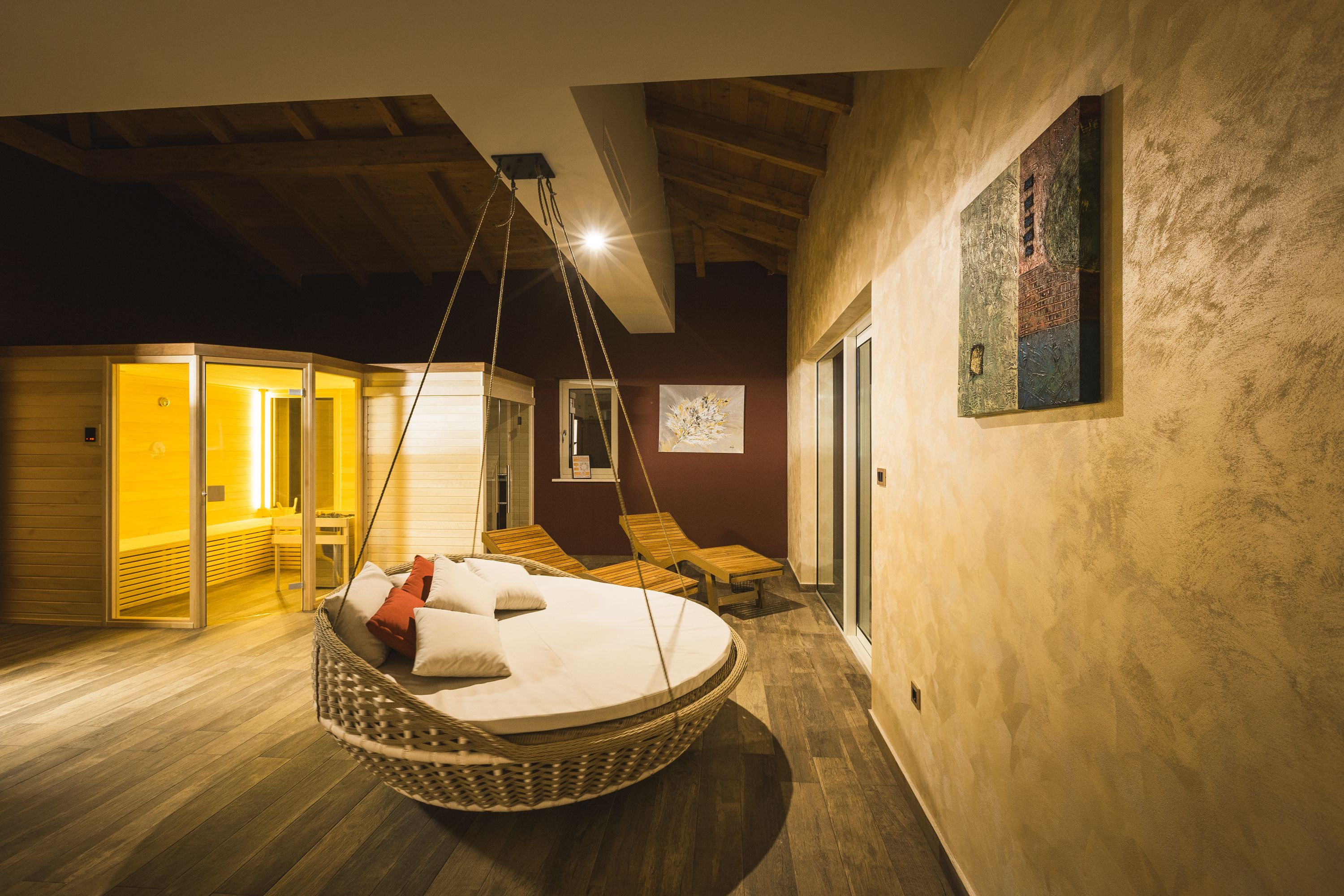 A room with a hanging chair, wooden flooring, and a bed with pillows.