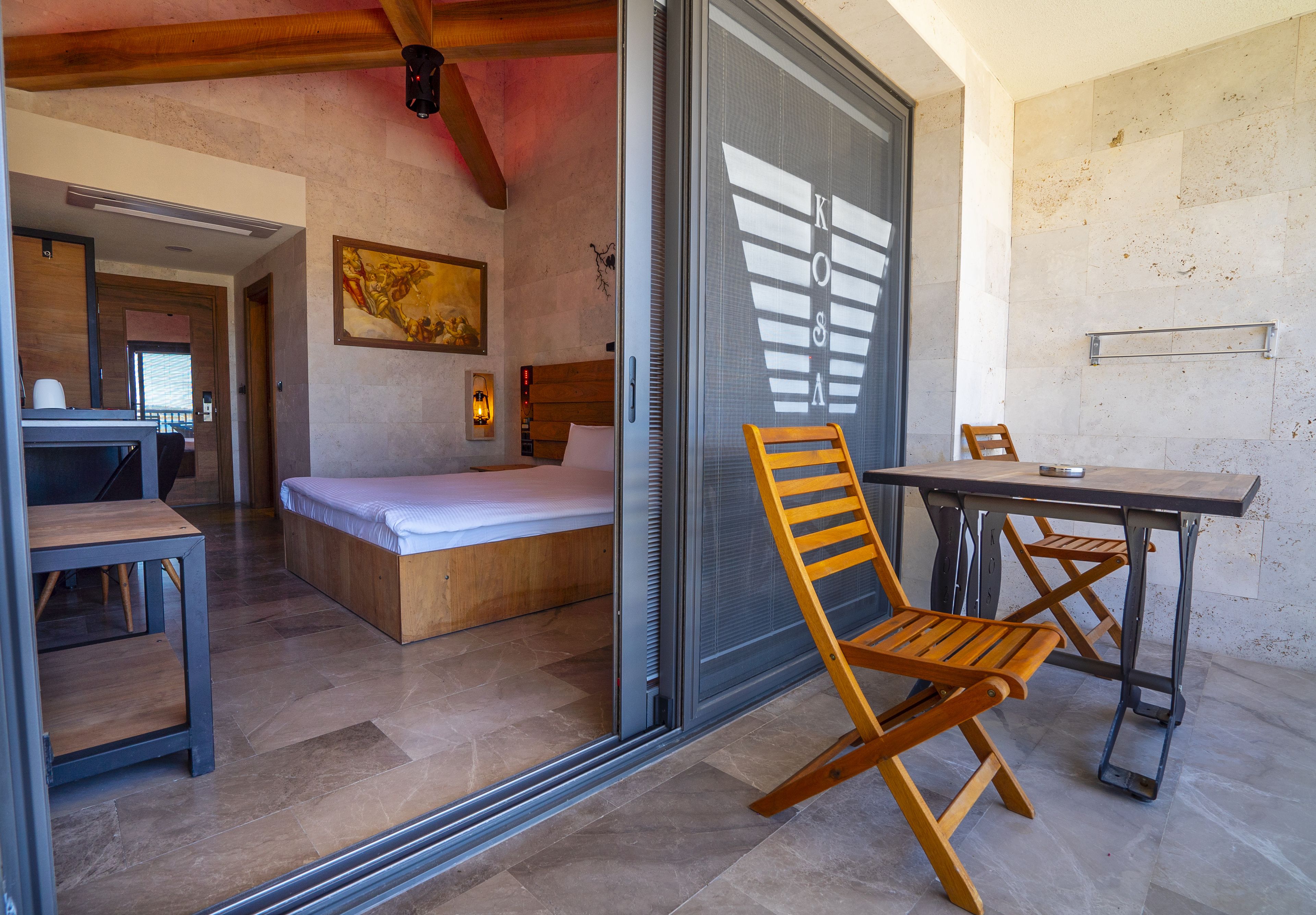 Un dormitorio moderno con una cama, una silla de madera, una mesa y un vidrio corredizo que da a un baño.
