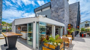 Un café al aire libre con barra, asientos y plantas en macetas.