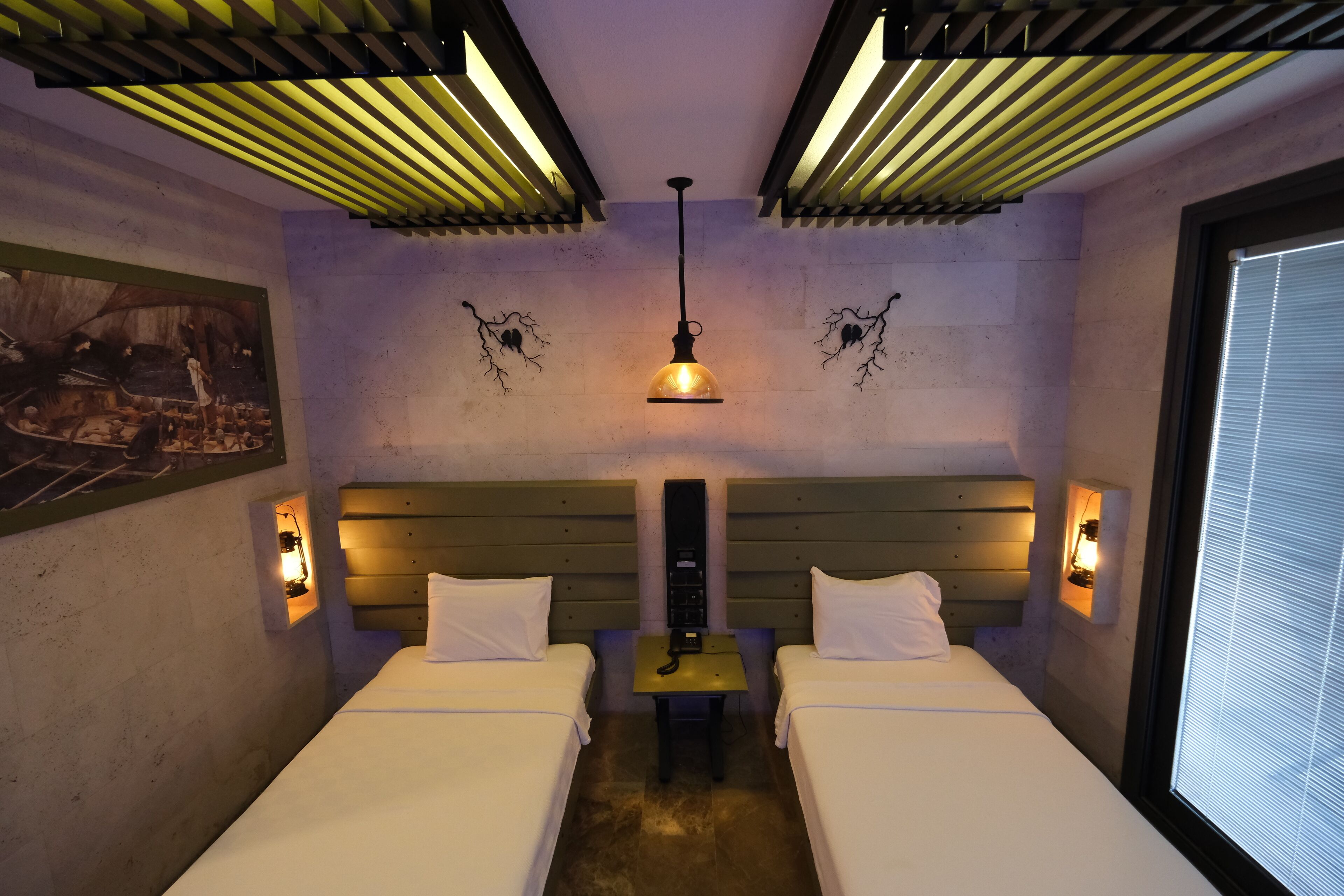 A hotel room with two beds, a central table, and a ceiling light fixture.