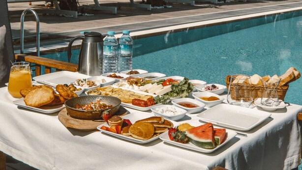 Zona de comedor junto a la piscina con una mesa dispuesta para el desayuno, con vistas a una piscina y sillones de descanso.