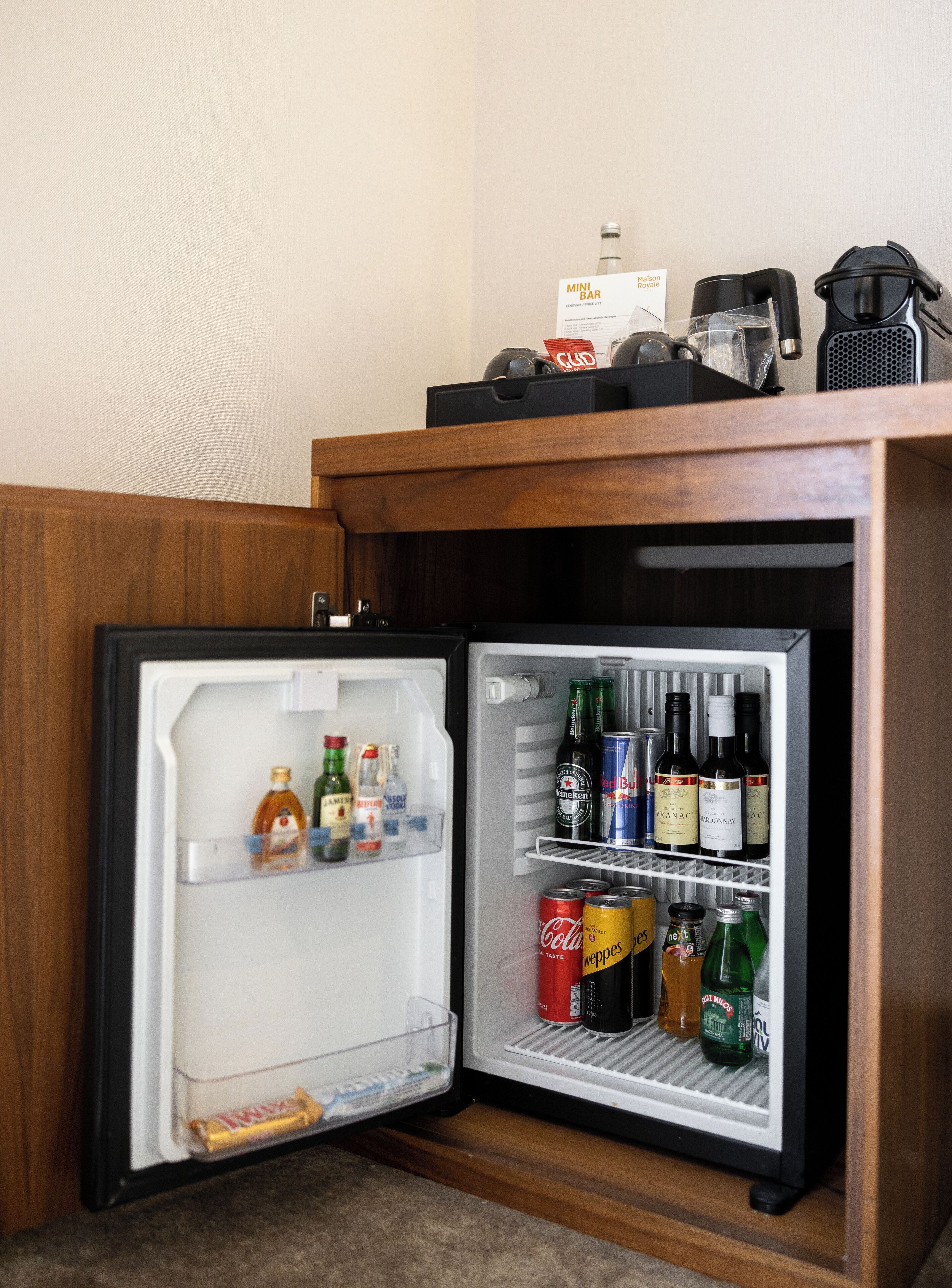 Eine Minikühlschrank mit Getränken und Snacks, darunter Weinflaschen, Bierdosen und eine Wasserflasche.