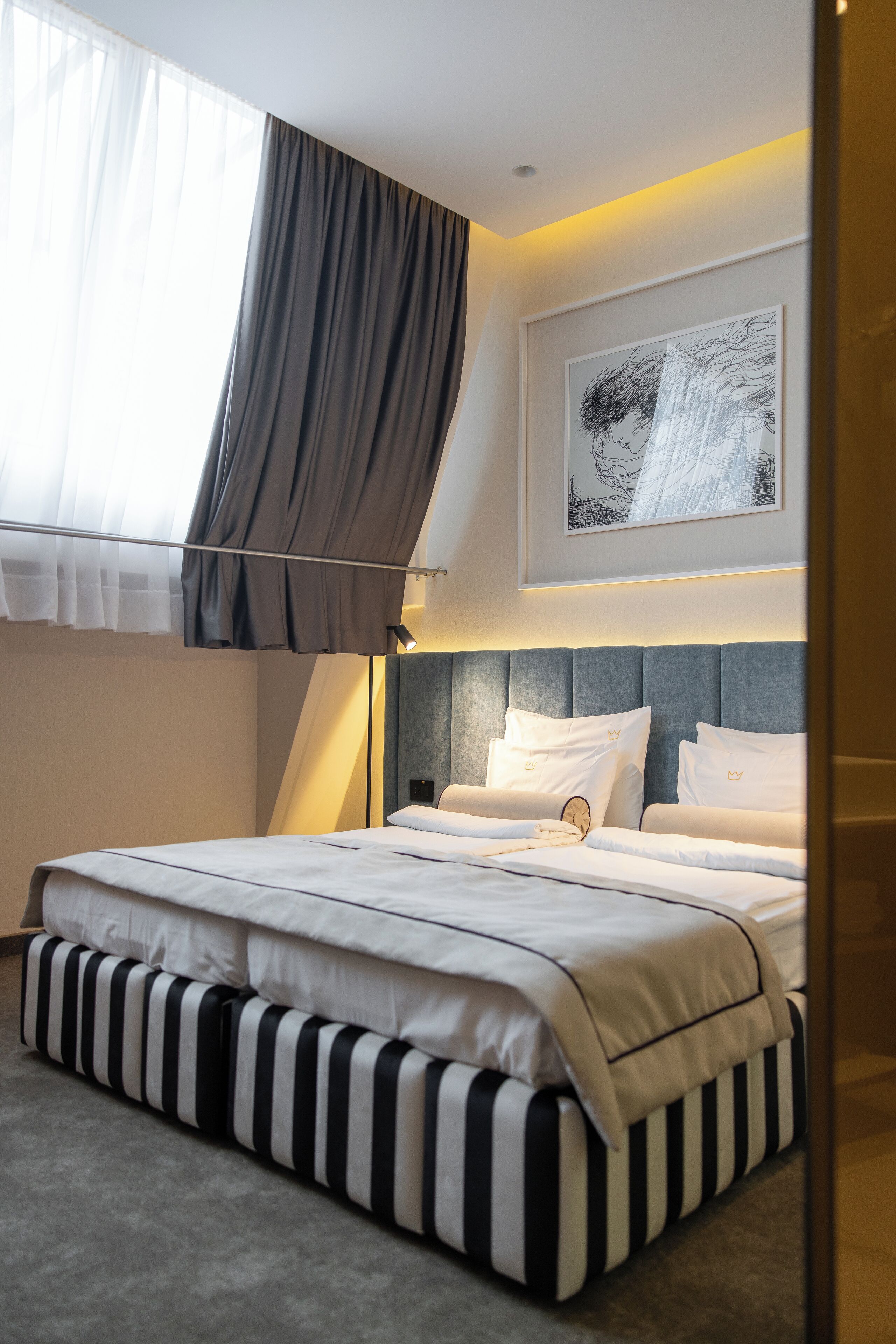 A modern hotel room with a large bed, a bedside table, a wall-mounted artwork, and a window with curtains.