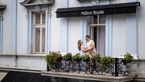 Una pareja en un balcón, con un letrero que dice "Maison Royale" en la parte superior.