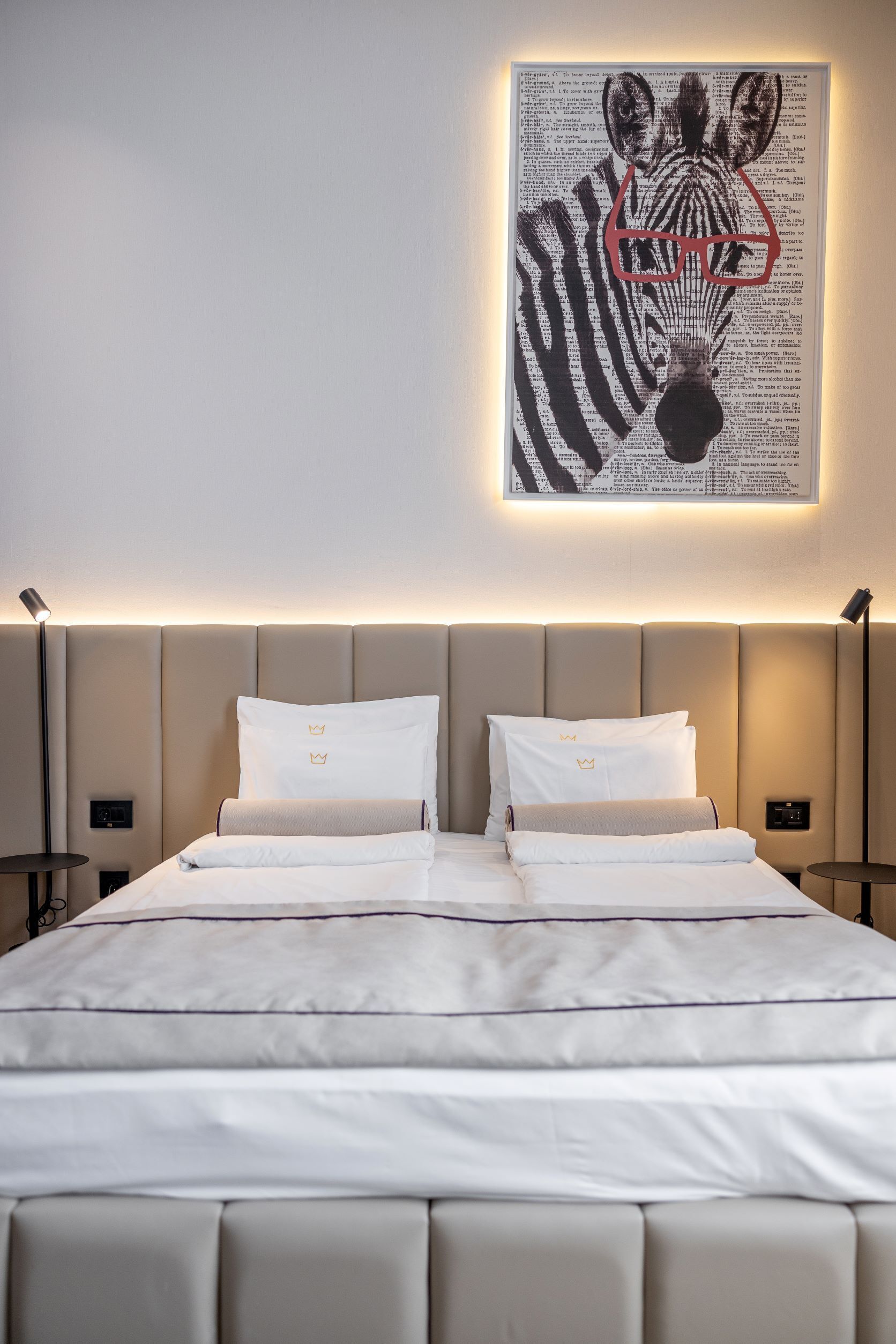 A modern hotel room with a large bed, two bedside tables, and a wall-mounted artwork.