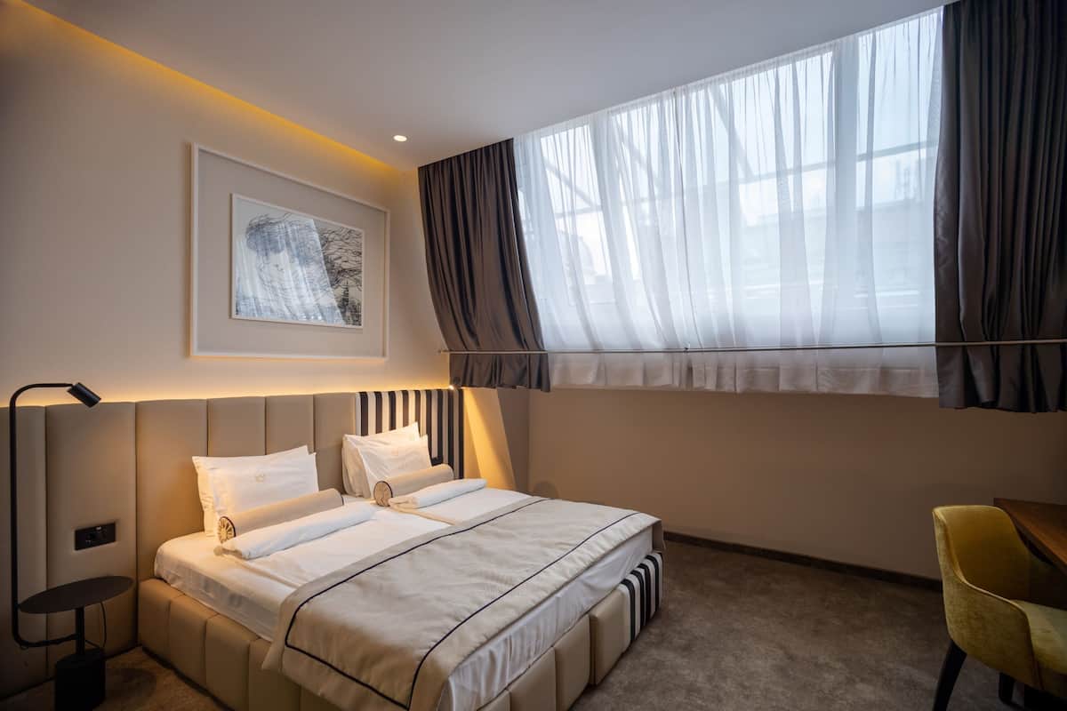 Ein modernes Hotelzimmer mit einem großen Bett, einem Nachttisch, einem Sessel und einem Fenster mit Vorhängen.