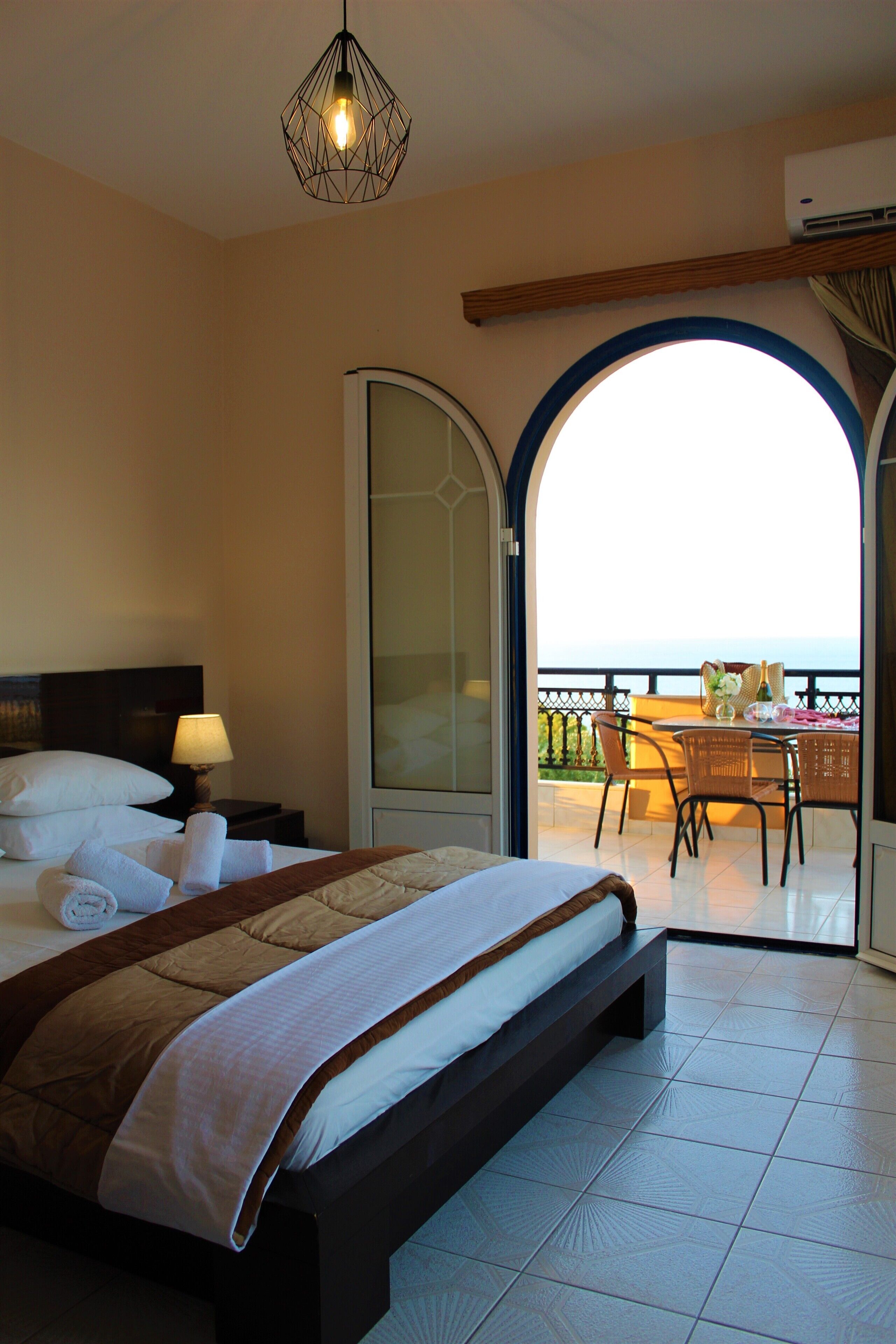 Camera d'albergo con un letto grande, un comodino con una lampada, un balcone con tavolo e sedie e vista sul mare.