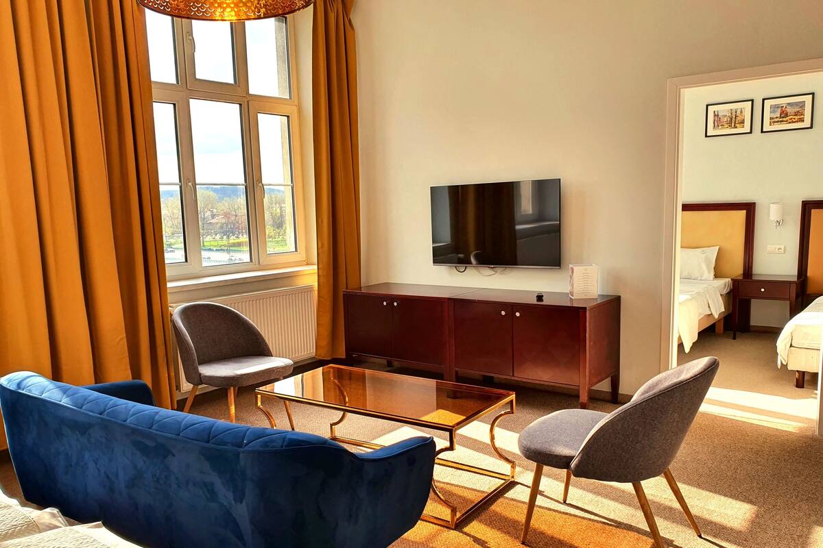 A hotel room with a large window, a flat-screen TV, a wooden cabinet, a blue sofa, and a grey armchair.
