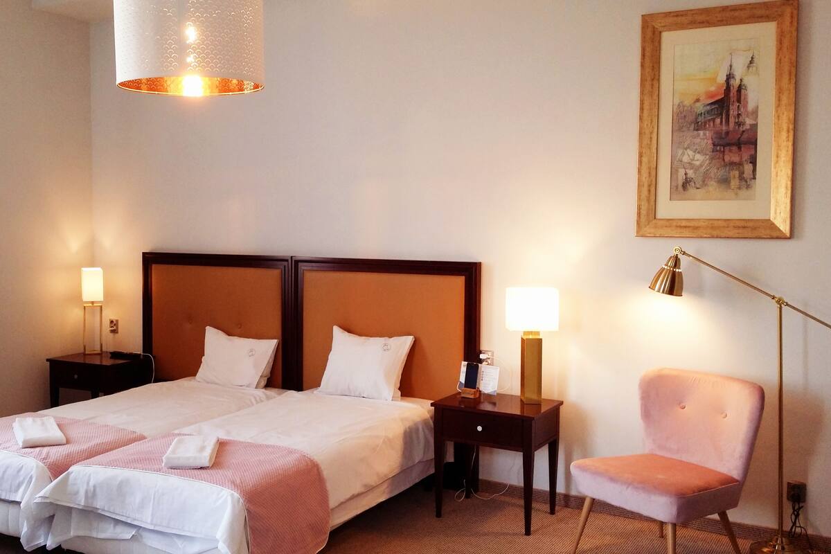 A hotel room with two beds, a chair, a desk, and a painting on the wall.