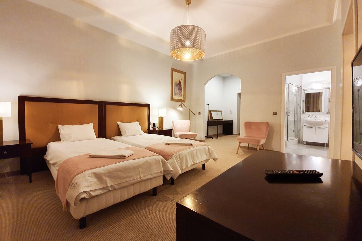 A hotel room with two beds, a desk, a chair, a TV, and a bathroom visible through an open door.