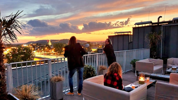 Une terrasse sur le toit avec des sièges extérieurs, une vue sur le paysage urbain au coucher du soleil et une rambarde.