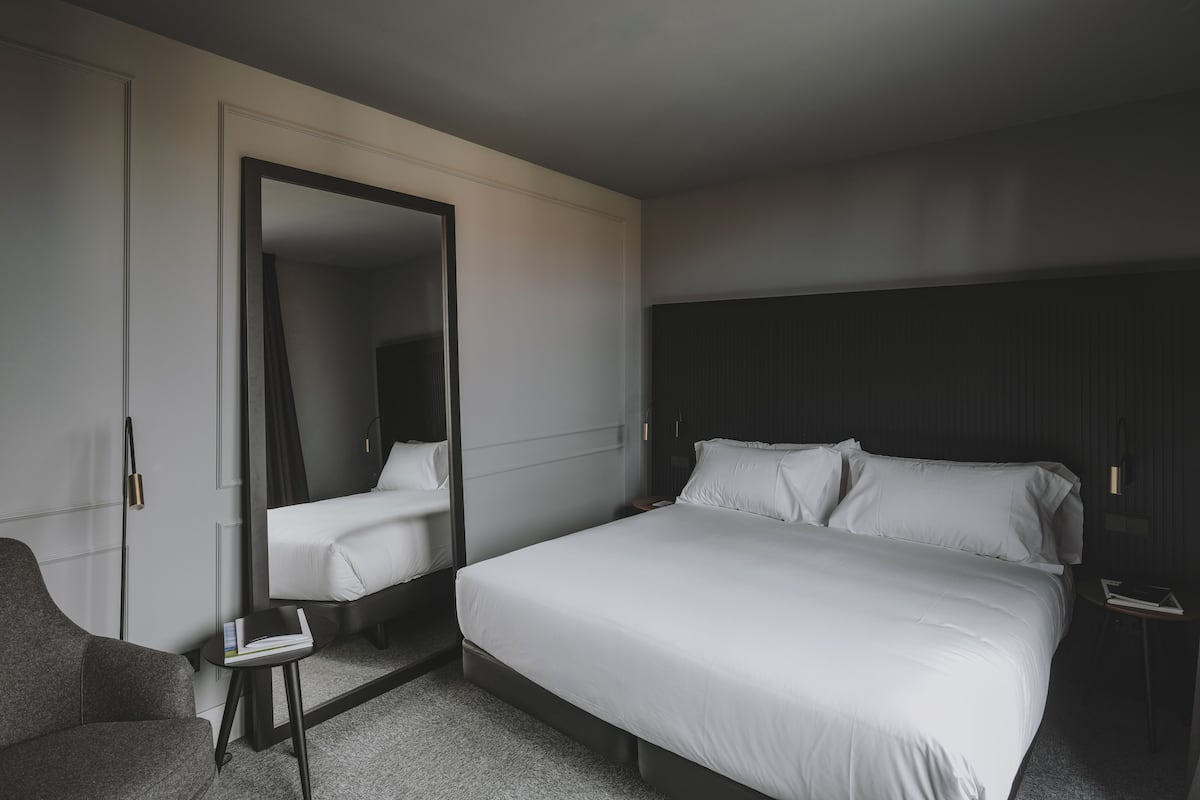 Ein Hotelzimmer mit einem großen Bett, einem Sessel, einem kleinen Tisch und einem Spiegel.