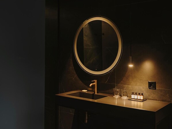 Un baño moderno con un espejo redondo, un lavamanos individual y una pequeña variedad de artículos de tocador.