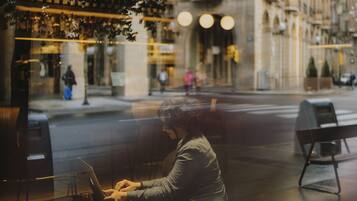 A person using a laptop at a table with a view of a street and buildings.