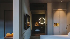 A modern hotel room with a bed, a desk, a mirror, and a vanity with a round mirror. - El Môderne Hotel Urban & Unique (Gijon)