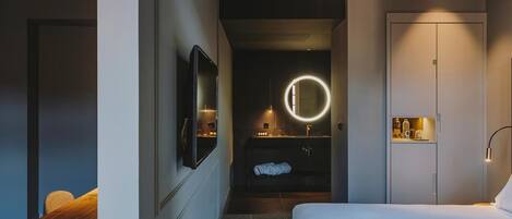 A modern hotel room with a bed, a desk, a mirror, and a vanity with a round mirror.