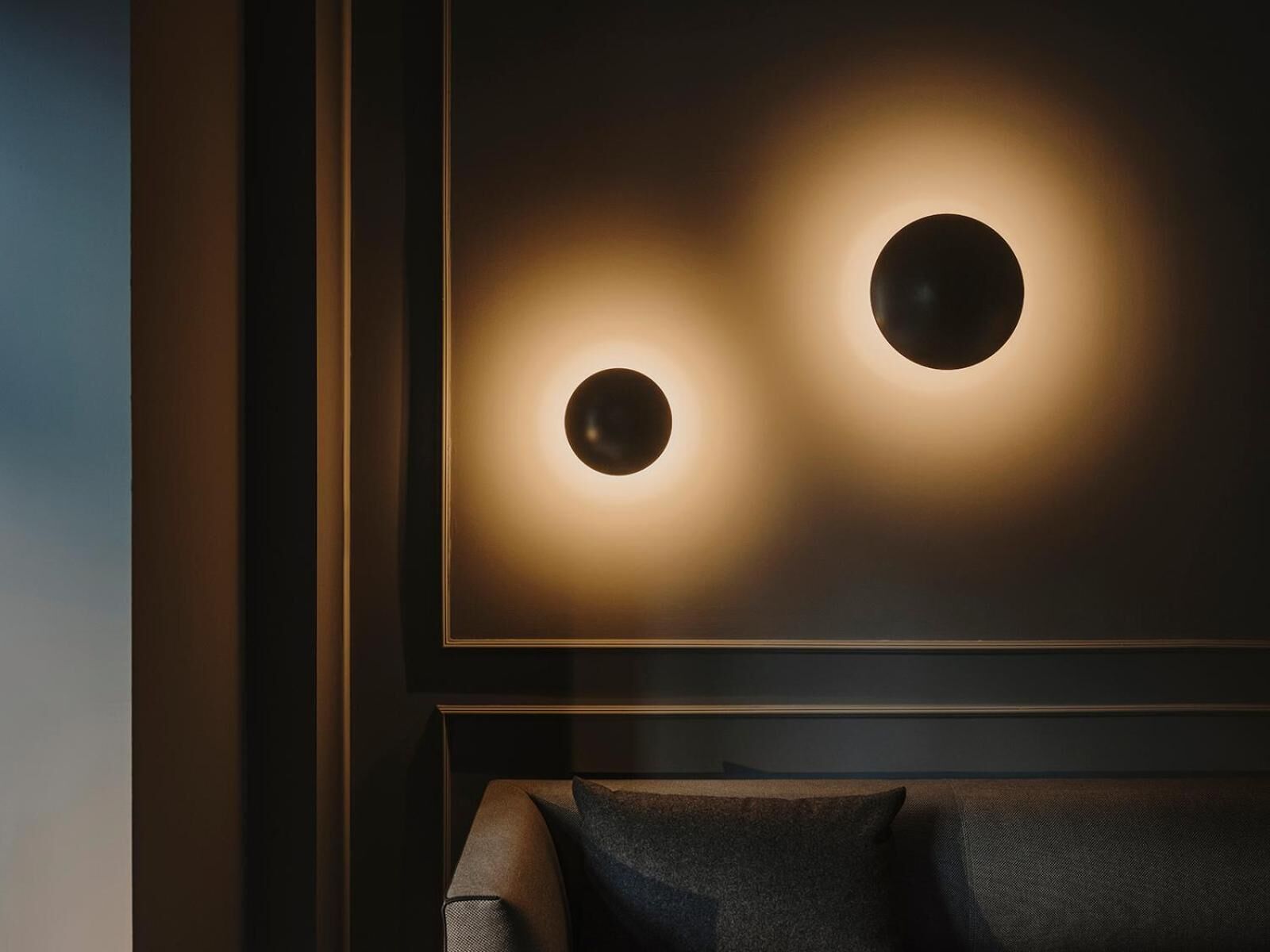 Una habitación moderna con una pared oscura y una obra de arte enmarcada que presenta dos fuentes de luz circulares.