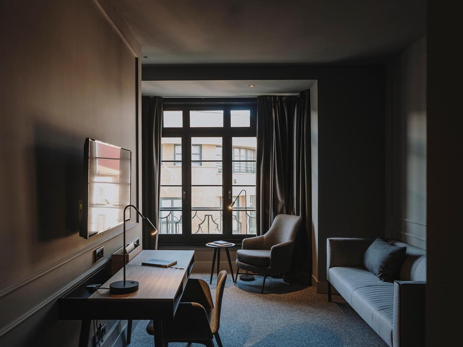 A hotel room with a desk, chair, sofa, and a TV.