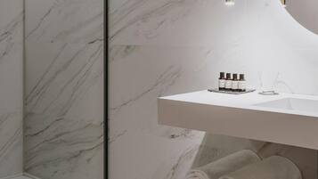 Un baño moderno con pared de mármol, un espejo redondo, un lavamanos blanco y zona de ducha.
