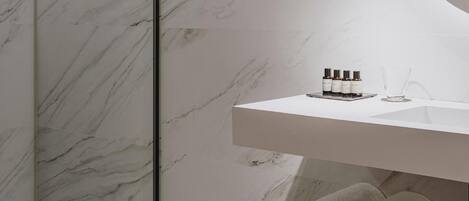 A modern bathroom with a marble wall, a round mirror, a white sink, and a shower area.