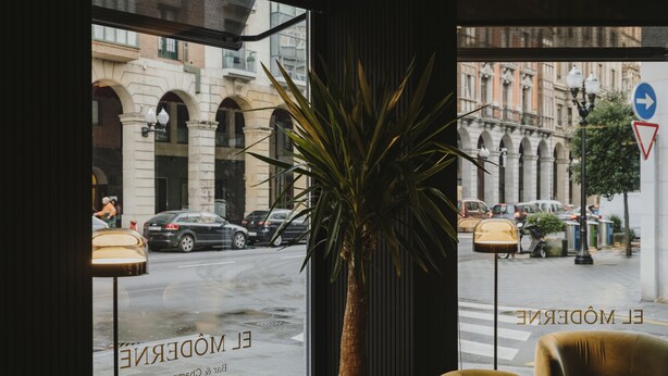 A view from a window with a potted plant, a street view, and a sign with "EL MODERE" and "BIS" visible. - El Môderne Hotel Urban & Unique (Gijon)