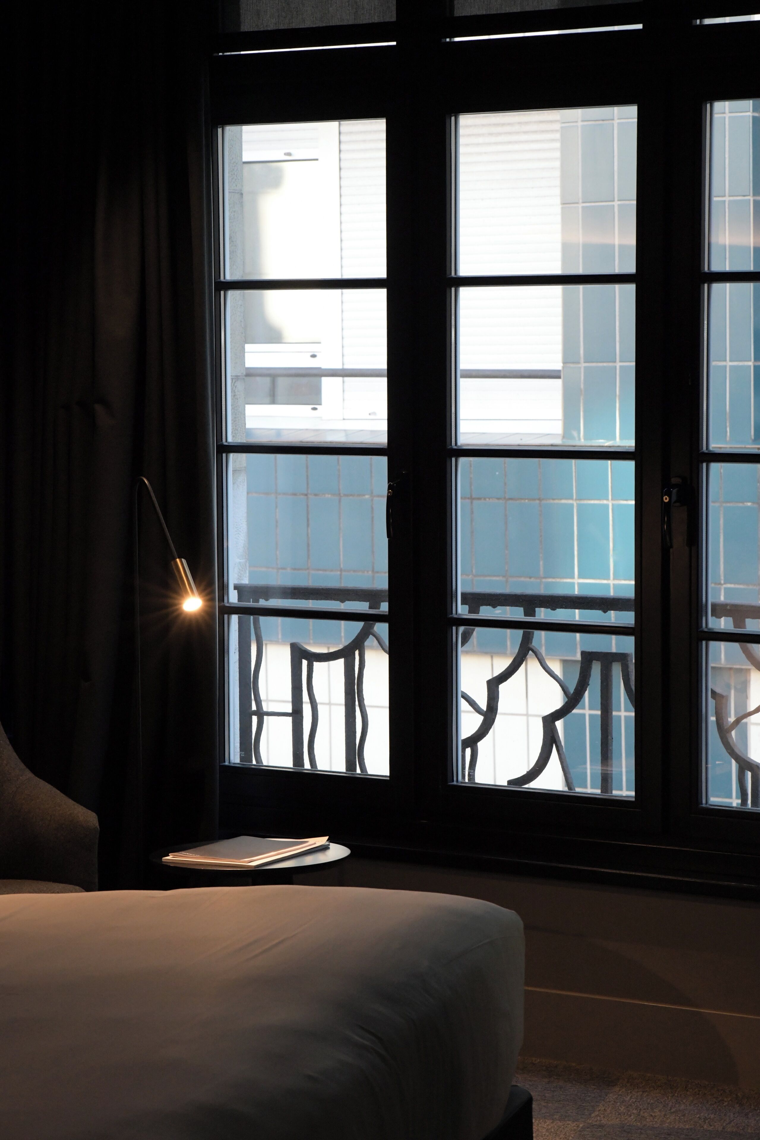 Et hotelværelse med et stort vindue, en seng, et natbord og en lampe.
