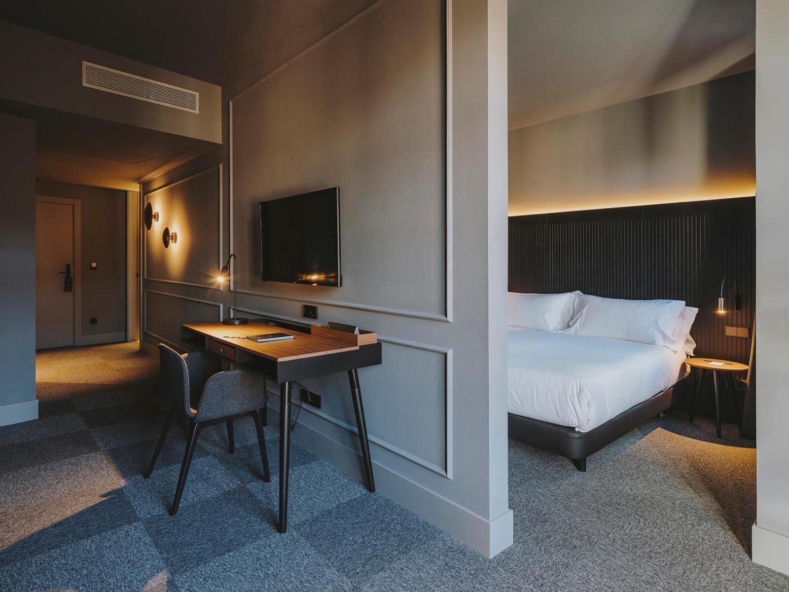 A modern hotel room with a bed, a desk, and a television.