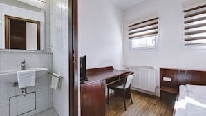 A small, clean room with a wooden desk, a chair, a radiator, and a window with blinds. - Hotel Filoxenia (Stuttgart)