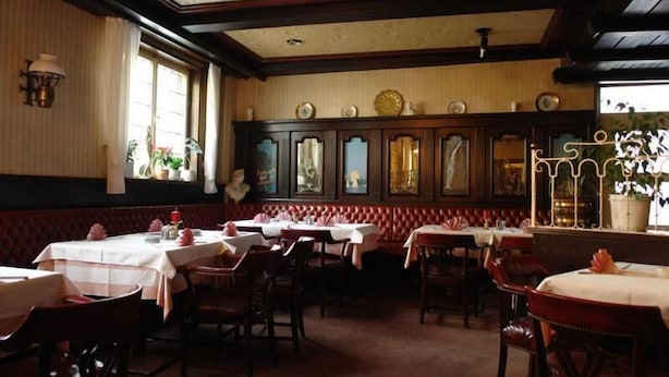 A restaurant with multiple tables and booths, wooden paneling, and a classic interior design. - Hotel Filoxenia (Stuttgart)