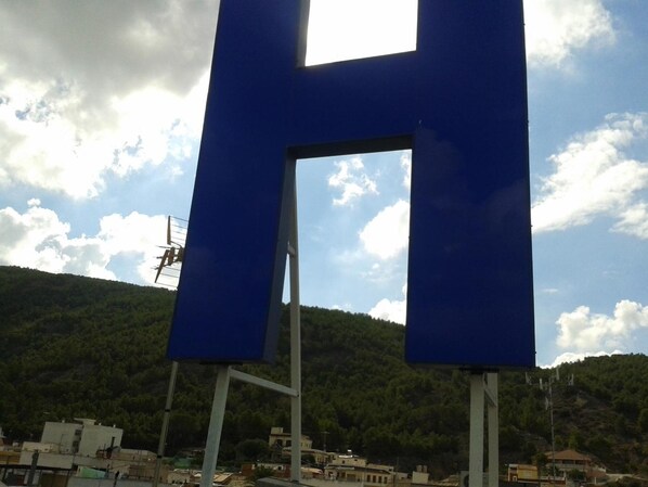 Una gran estructura azul en forma de H, con cielo despejado y montañas al fondo.