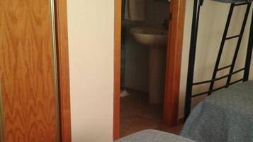 A small, compact room with a bunk bed and a single bed. A wooden door and a small window are visible.