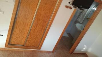 Een kamer met een houten garderobe, een aan de muur bevestigde televisie en een badkamer zichtbaar door een geopende deur.