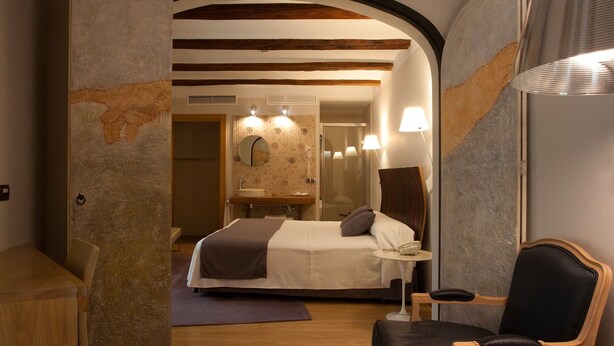 A modern hotel room with a large bed, a small table, a chair, and a mirror. - Hospederia Chapitel (Estella)