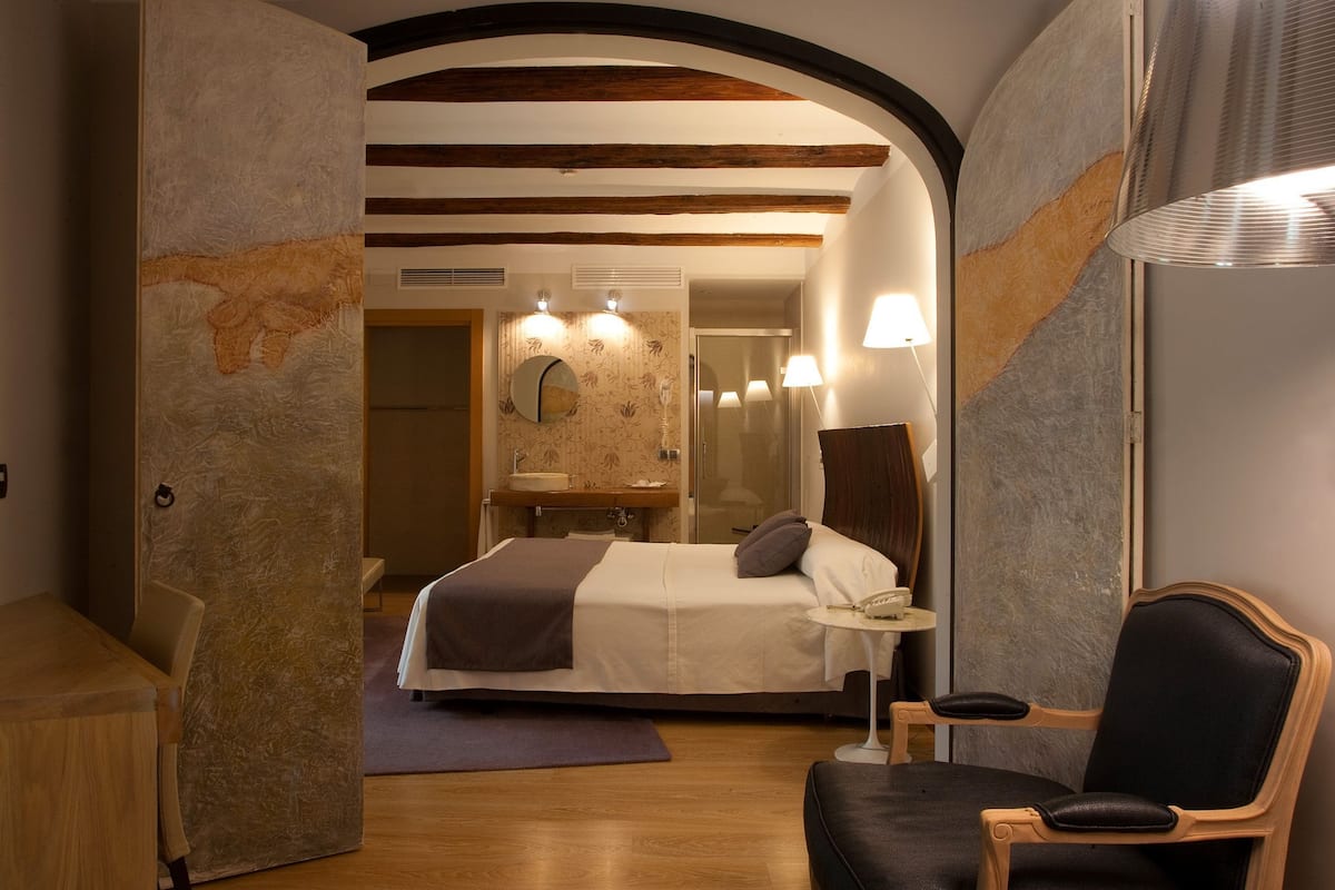 Ein modernes Hotelzimmer mit einem großen Bett, einem kleinen Tisch, einem Stuhl und einem Spiegel.