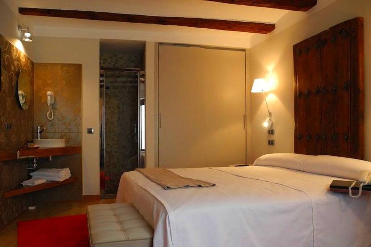 Ein Schlafzimmer mit Bett, Nachttisch, rotem Teppich, Holz-Kopfstütze und einem Badezimmer mit Waschbecken und Spiegel.