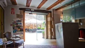 A room with a wooden ceiling, a glass door leading outside, a chair, a small table, and a refrigerator. - Hospederia Chapitel (Estella)
