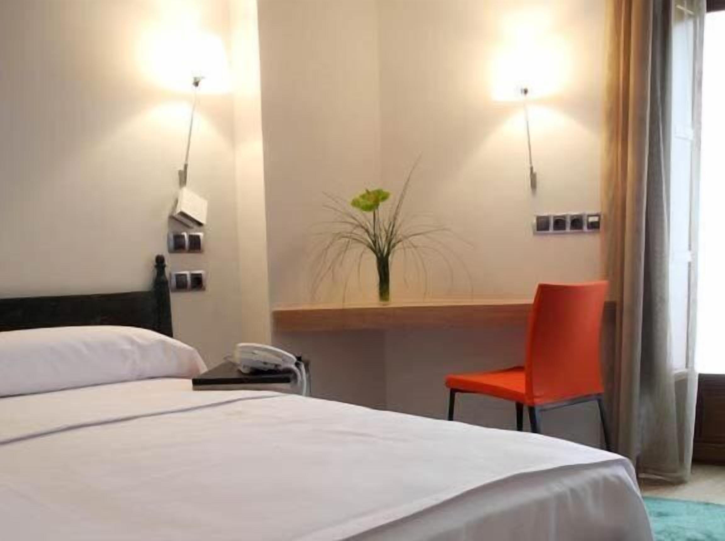 Una habitación de hotel con una cama, un escritorio, una silla y un florero con una planta.