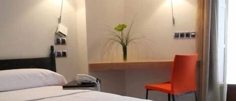 Una habitación de hotel con una cama, un escritorio, una silla y un florero con una planta.
