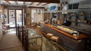 A restaurant with a bar area, wooden furniture, and a stone wall. - Hospederia Chapitel (Estella)