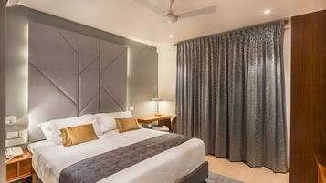 Una habitación de hotel moderna con una cama grande, un ventilador de techo, una mesita de noche con lámpara y una ventana con cortinas.
