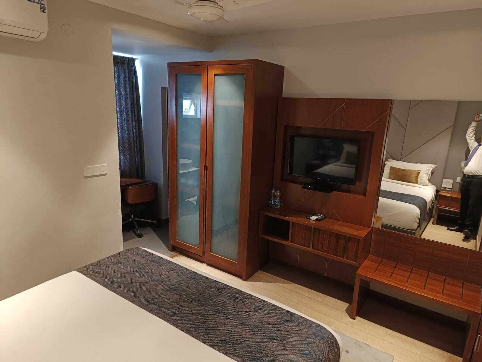 A hotel room with a bed, a TV, a wardrobe, a desk, and a chair.