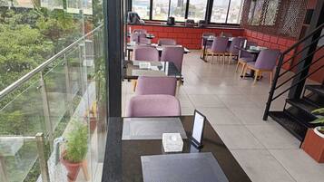 Un espace de détente intérieur moderne, doté de tables et de chaises, de grandes fenêtres et offrant une vue sur la verdure environnante.
