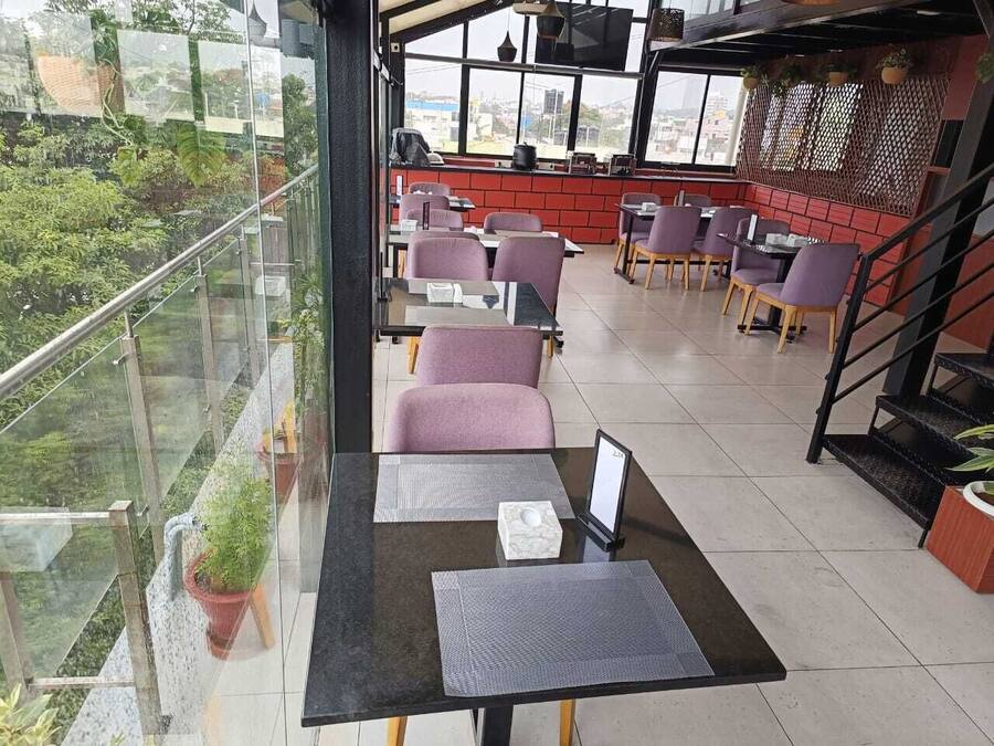 Un espace de détente intérieur moderne, doté de tables et de chaises, de grandes fenêtres et offrant une vue sur la verdure environnante.