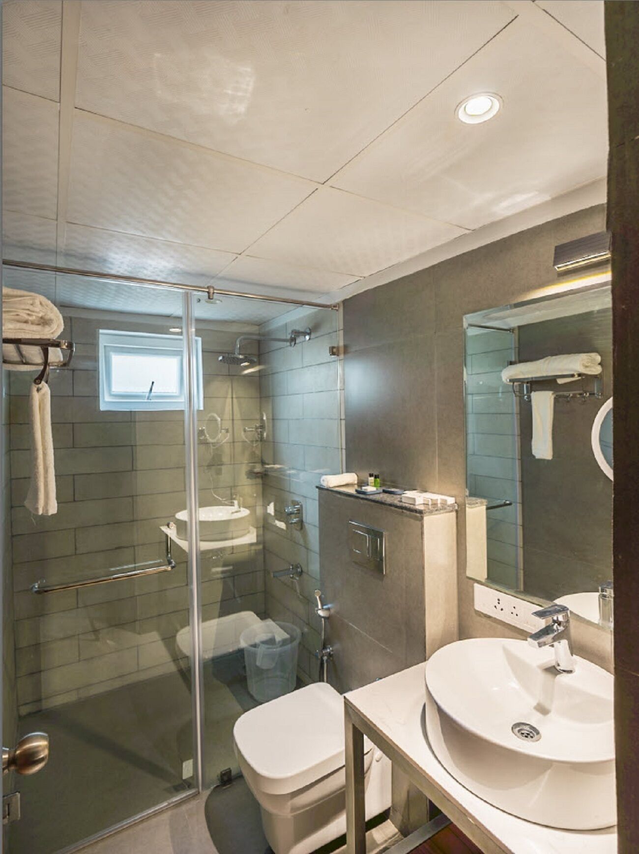 Un baño moderno con ducha envuelta en vidrio, un lavamanos blanco y un espejo grande.