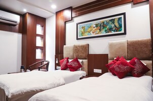 Habitación de hotel con dos camas, ropa de cama roja y blanca, un cuadro abstracto enmarcado y un cabecero de madera.