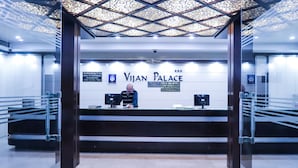 Un comptoir d’accueil à l’hôtel Vijan Palace, doté d’un design moderne, avec un plafond orné de motifs et une enseigne indiquant l’emplacement de la réception.