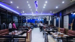 Un restaurant doté de tables hautes et de banquettes, offrant une vue sur le paysage urbain et présentant un décor intérieur moderne.