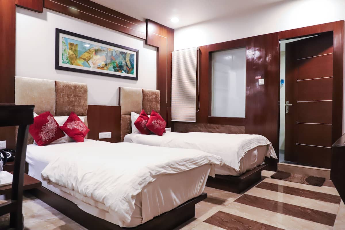 Une chambre d’hôtel avec deux lits, un tableau au mur, une fenêtre avec des stores et une porte en bois.