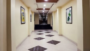 Un couloir au sol décoré de motifs, avec des tableaux encadrés accrochés aux murs et un escalier au fond.
